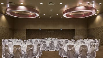 Uma sala de banquetes com mesas redondas, toalhas brancas e cadeiras com fitas brancas.