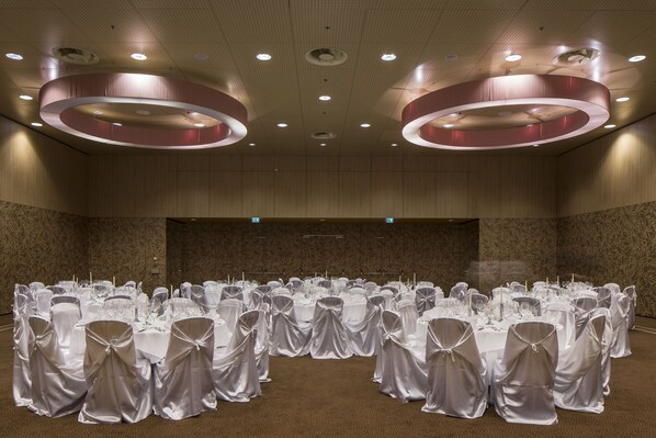 A banquet hall with round tables, white tablecloths, and chairs with white sashes.