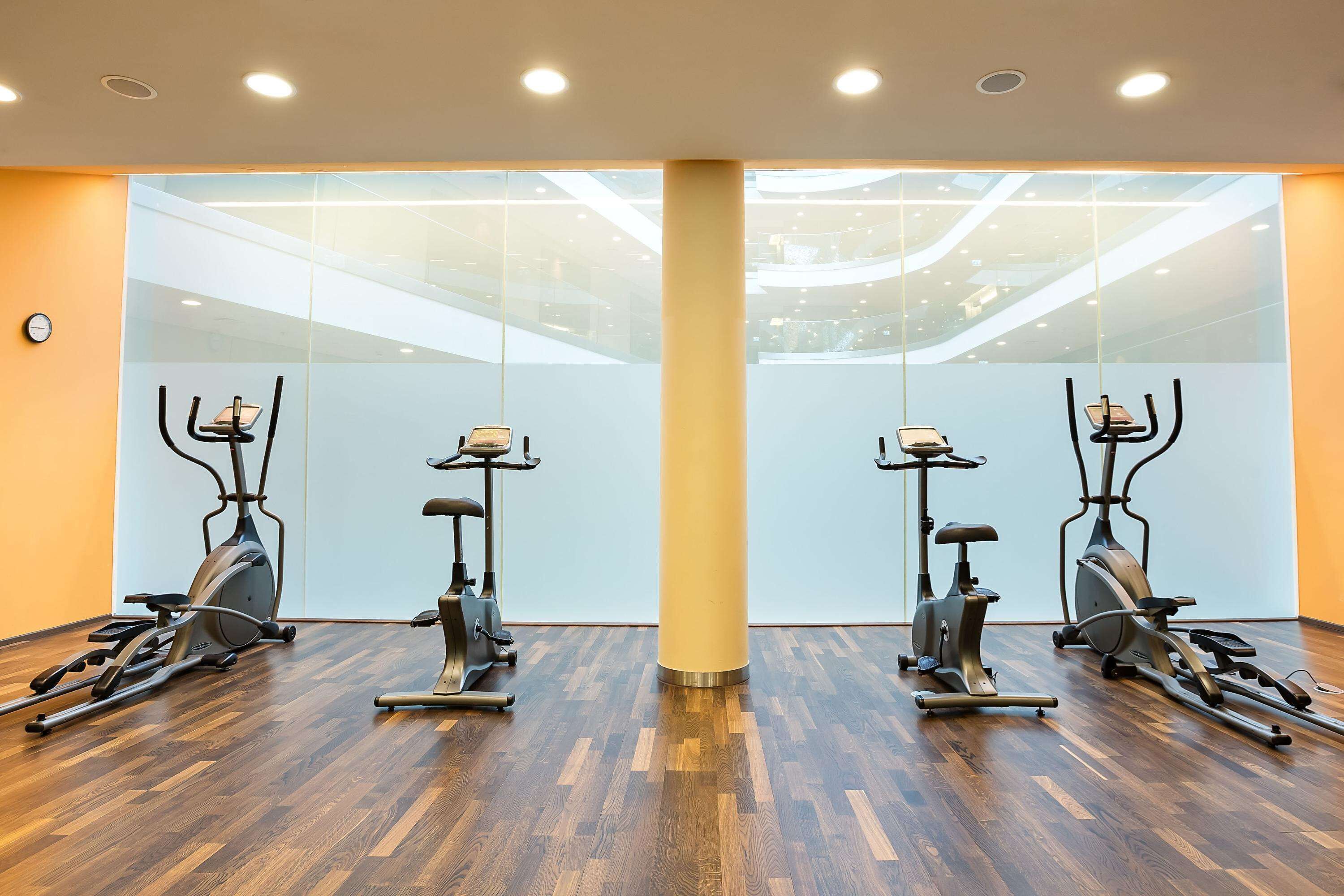 Un gimnasio con paredes espejadas, piso de madera y equipamiento de ejercicio.