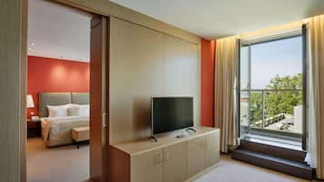 A hotel room with a bed, a TV on a wooden cabinet, a window with curtains, and a view of the outdoors.
