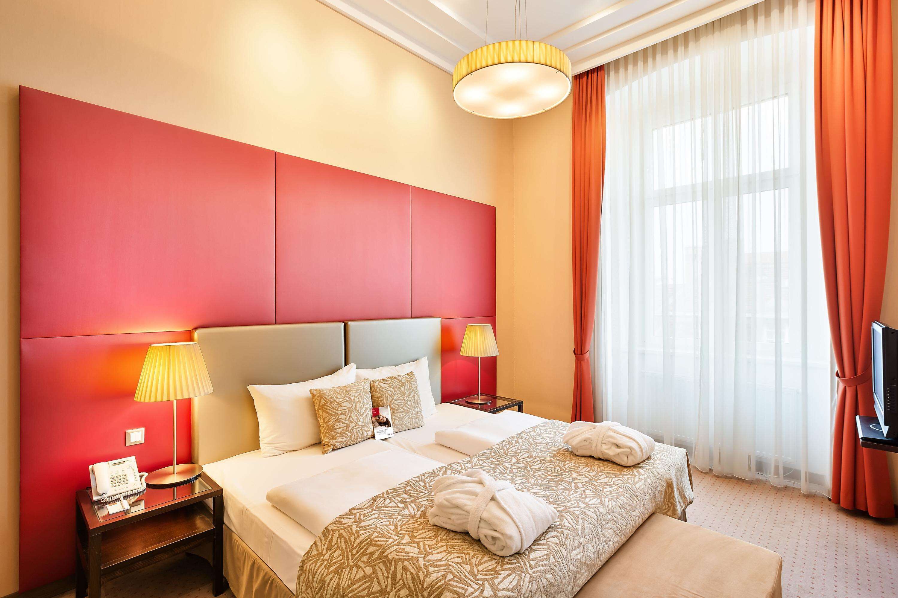 Quarto de hotel com uma cama grande, duas mesas de cabeceira, uma televisão e uma janela com cortinas.