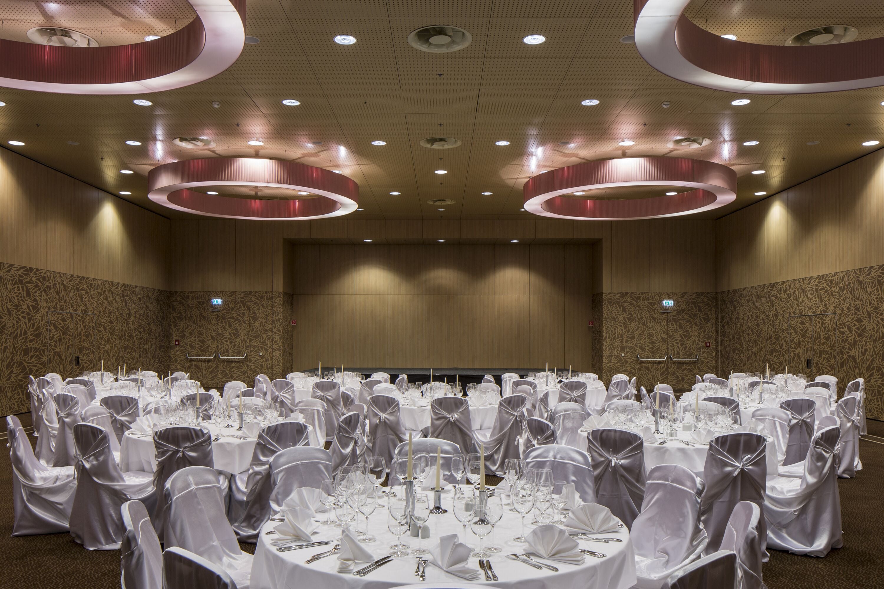 Un salón de banquetes con mesas redondas dispuestas para un evento formal, con manteles blancos, cubertería y cristalería.