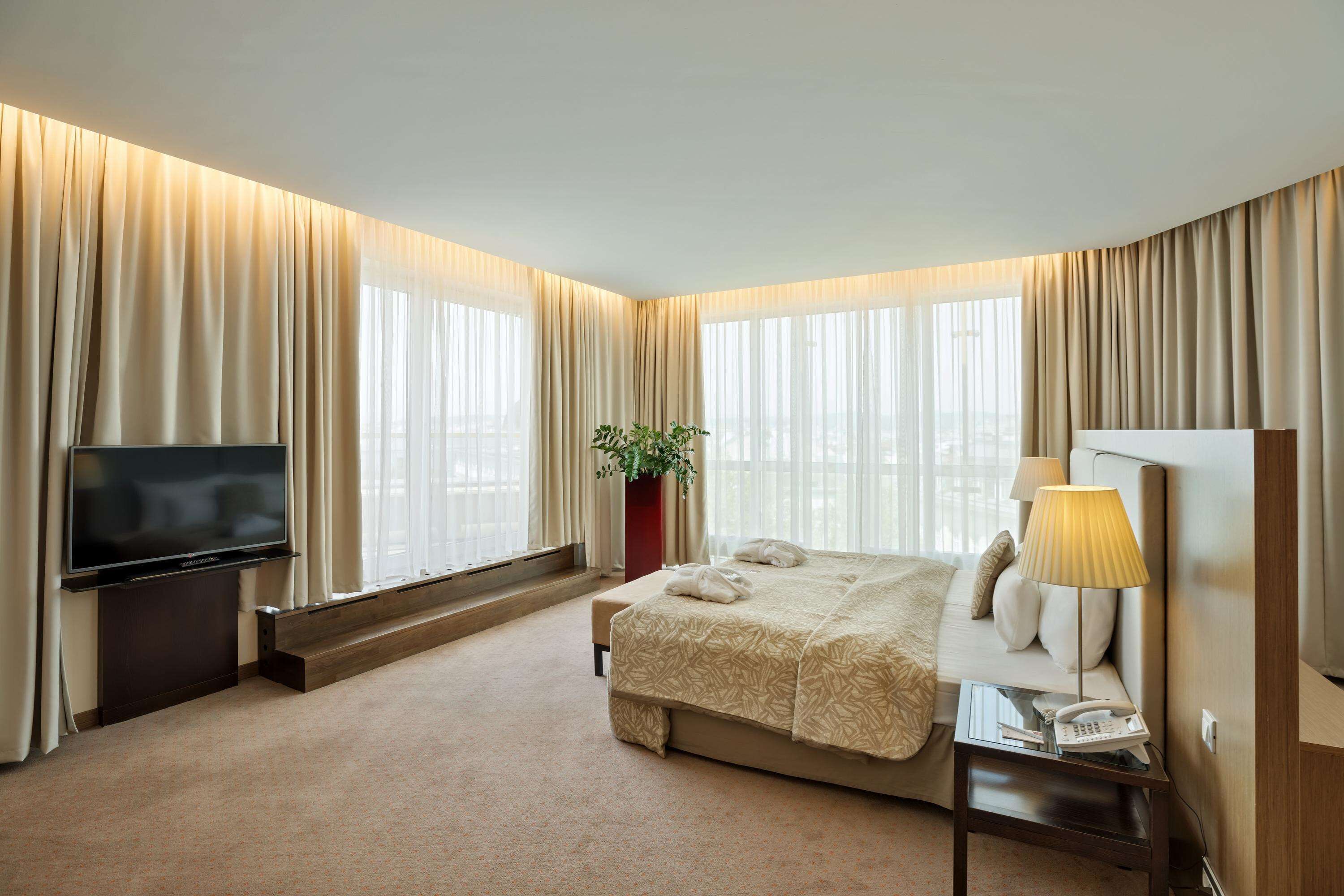 Ein Hotelzimmer mit einem großen Bett, einem Flachbildfernseher, einem Nachttisch mit Lampe und einer Pflanze.