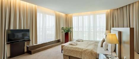 A hotel room with a large bed, a flat-screen TV, a bedside table with a lamp, and a plant.