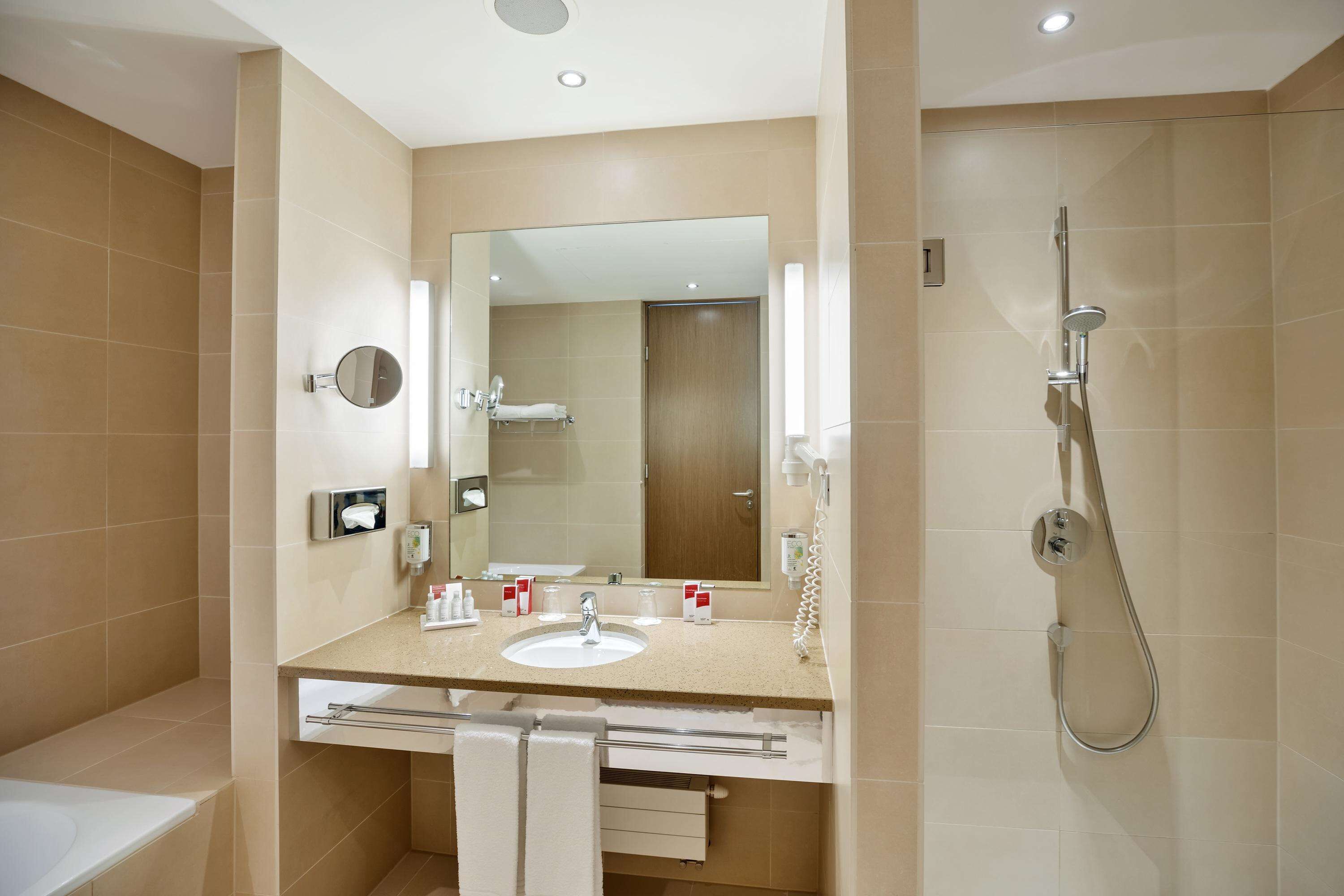 A modern bathroom with a large mirror, a sink, and a shower.