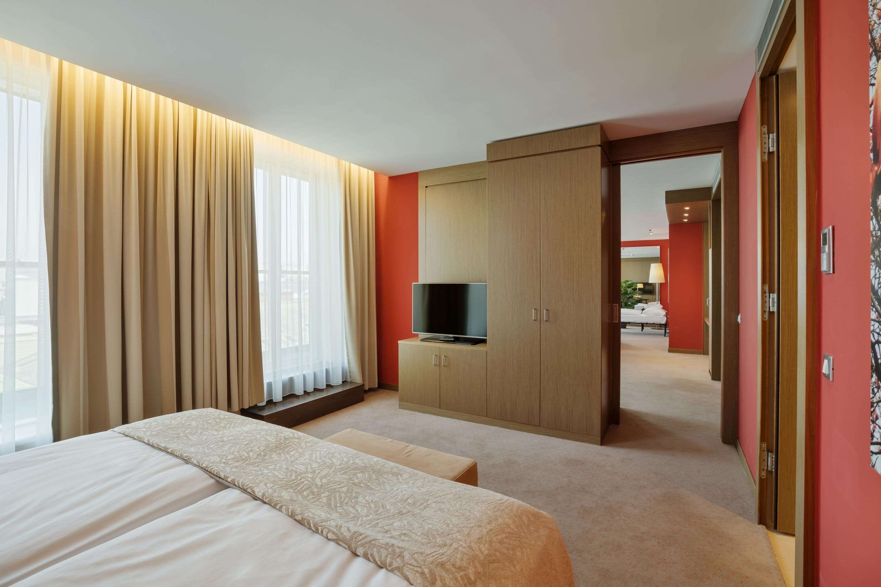 Una habitación de hotel con cama, televisor en un mueble de madera y vista al pasillo.