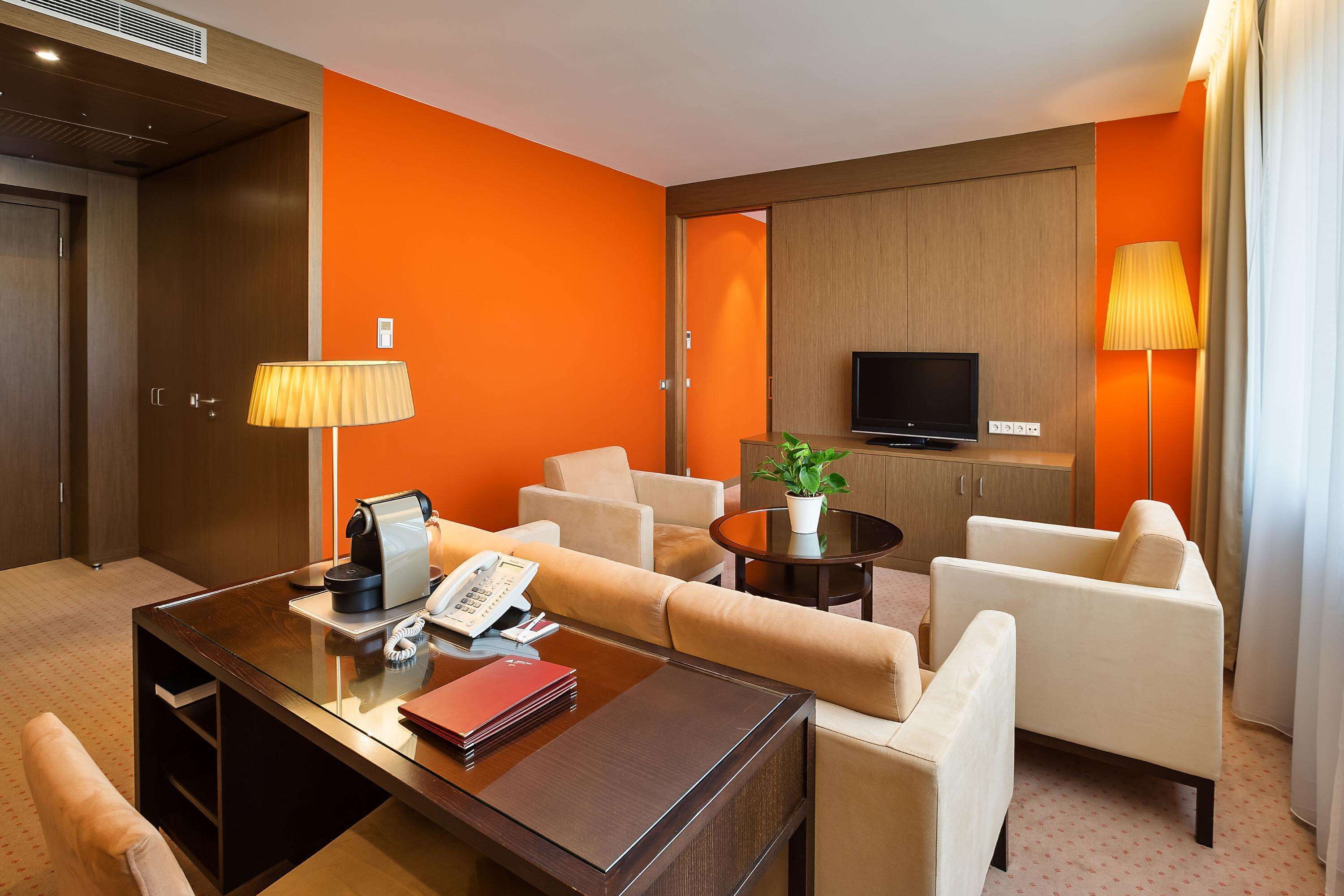 A hotel room with a wooden desk, a telephone, a lamp, a television, and a sofa.