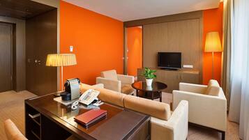 Ein Hotelzimmer mit einem Holztisch, einem Telefon, einer Lampe, einem Fernseher und einem Sofa.