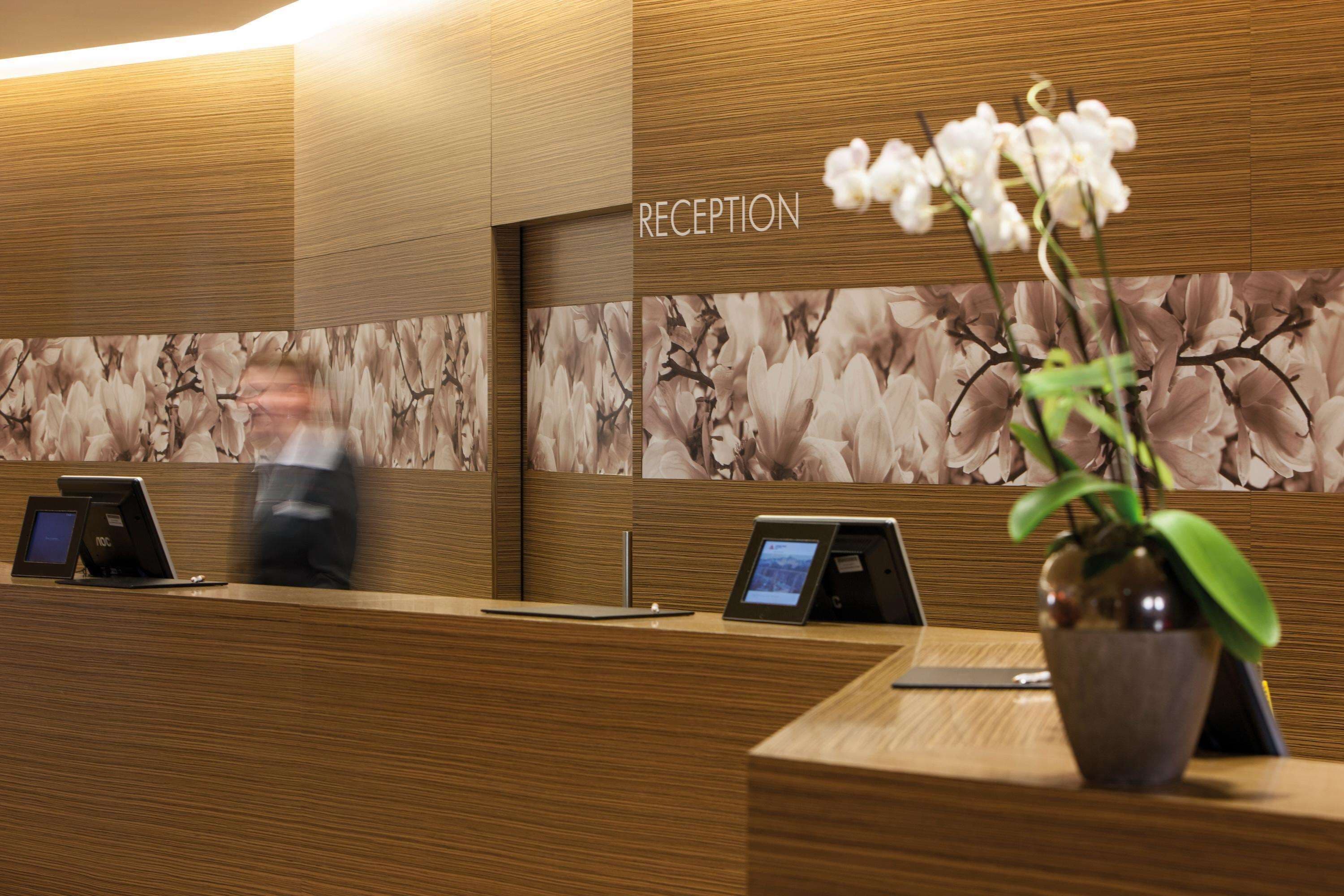 A reception desk with a floral wallpaper backdrop, a vase with white flowers, and a sign that reads "RECEPTION".