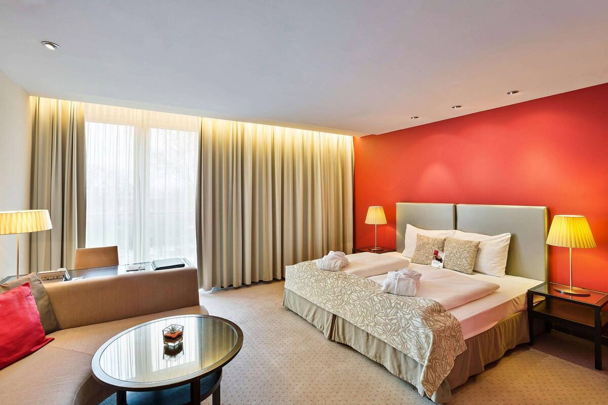 Een hotelkamer met een bed, een bank, een klein tafeltje en een nachtkastje met lampen.
