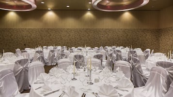 A banquet hall with round tables set for a formal event, featuring white tablecloths, silverware, and candle holders.