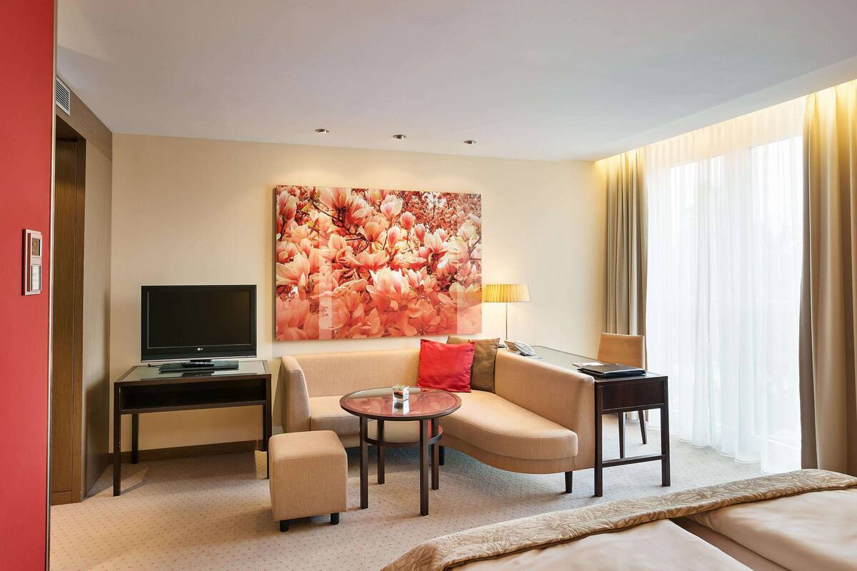 Een hotelkamer met een bank, een bijzettafeltje, een televisie op een standaard en een groot bloemdecoratief aan de muur.