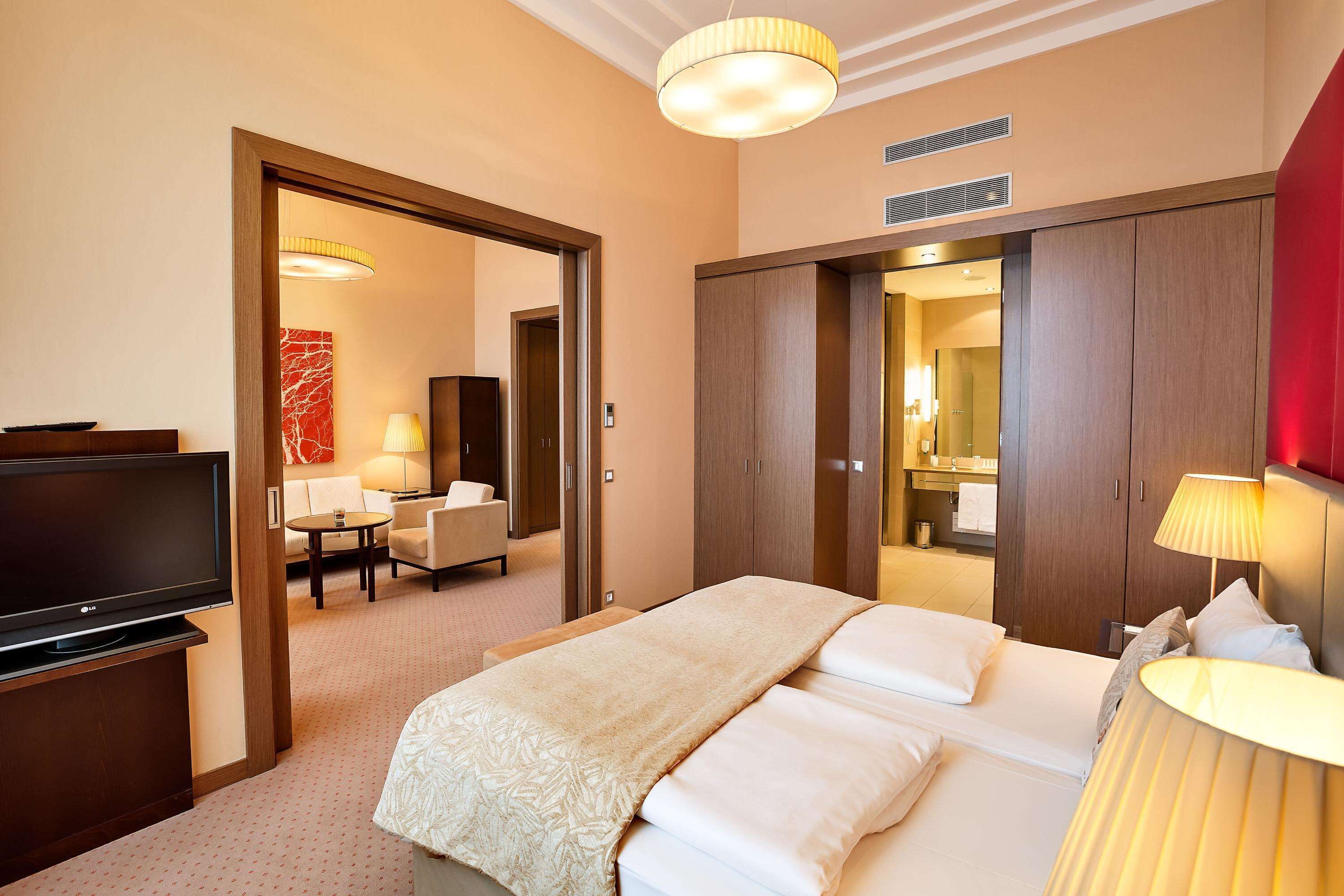Quarto de hotel com cama, abajures, televisão, escrivaninha e uma cadeira.