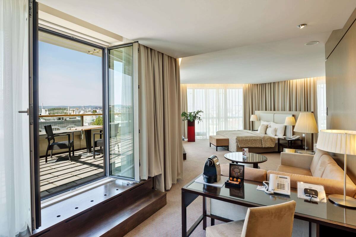 Een hotelkamer met een balkon, een sofa, een salontafel, een bureau en een bed.