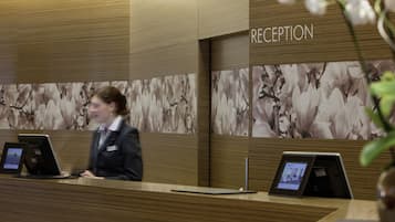A reception area with a wooden reception desk, a digital display, and a floral wallpaper backdrop.