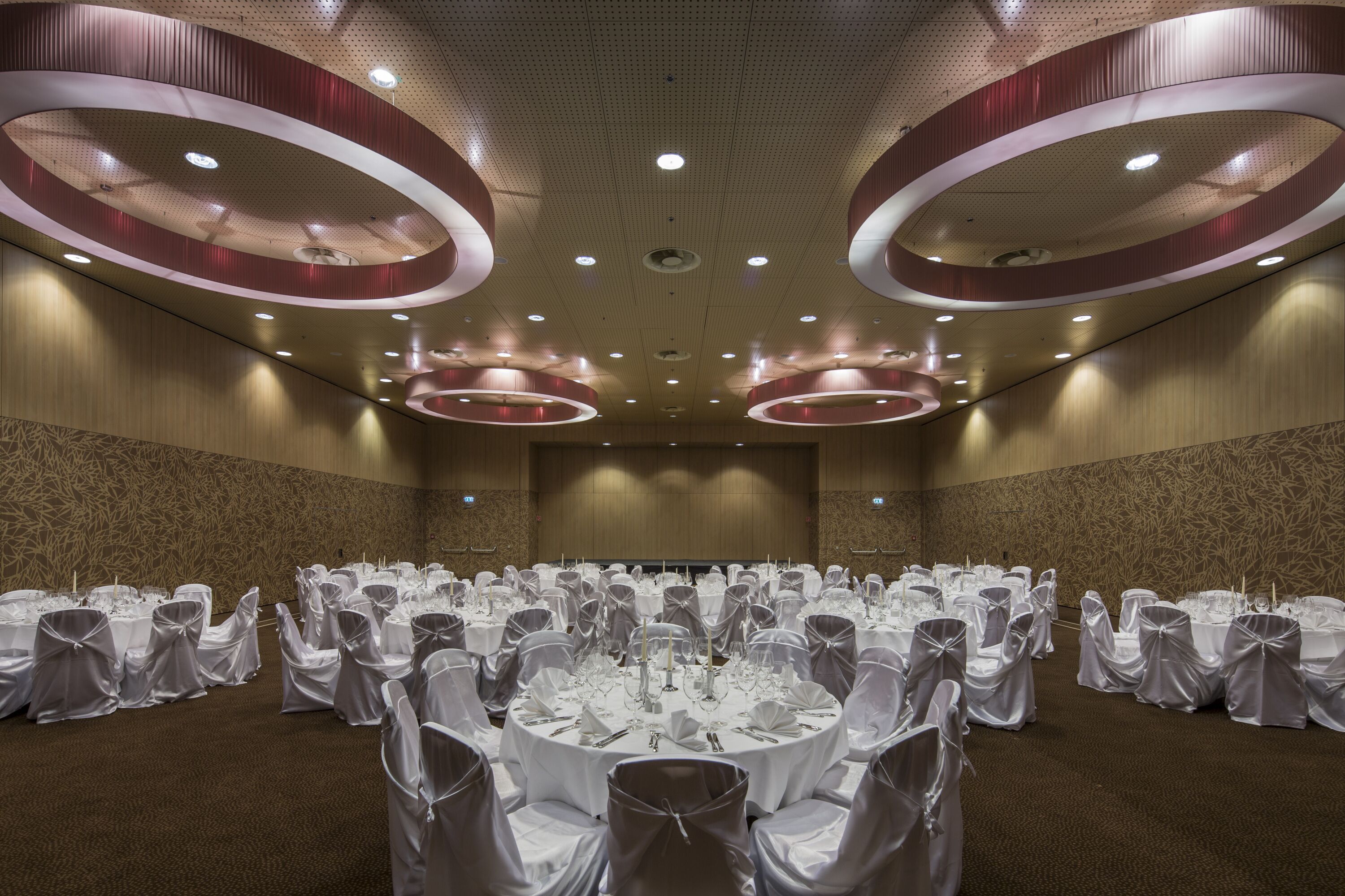 A banquet hall with round tables, white tablecloths, and chairs with white covers.