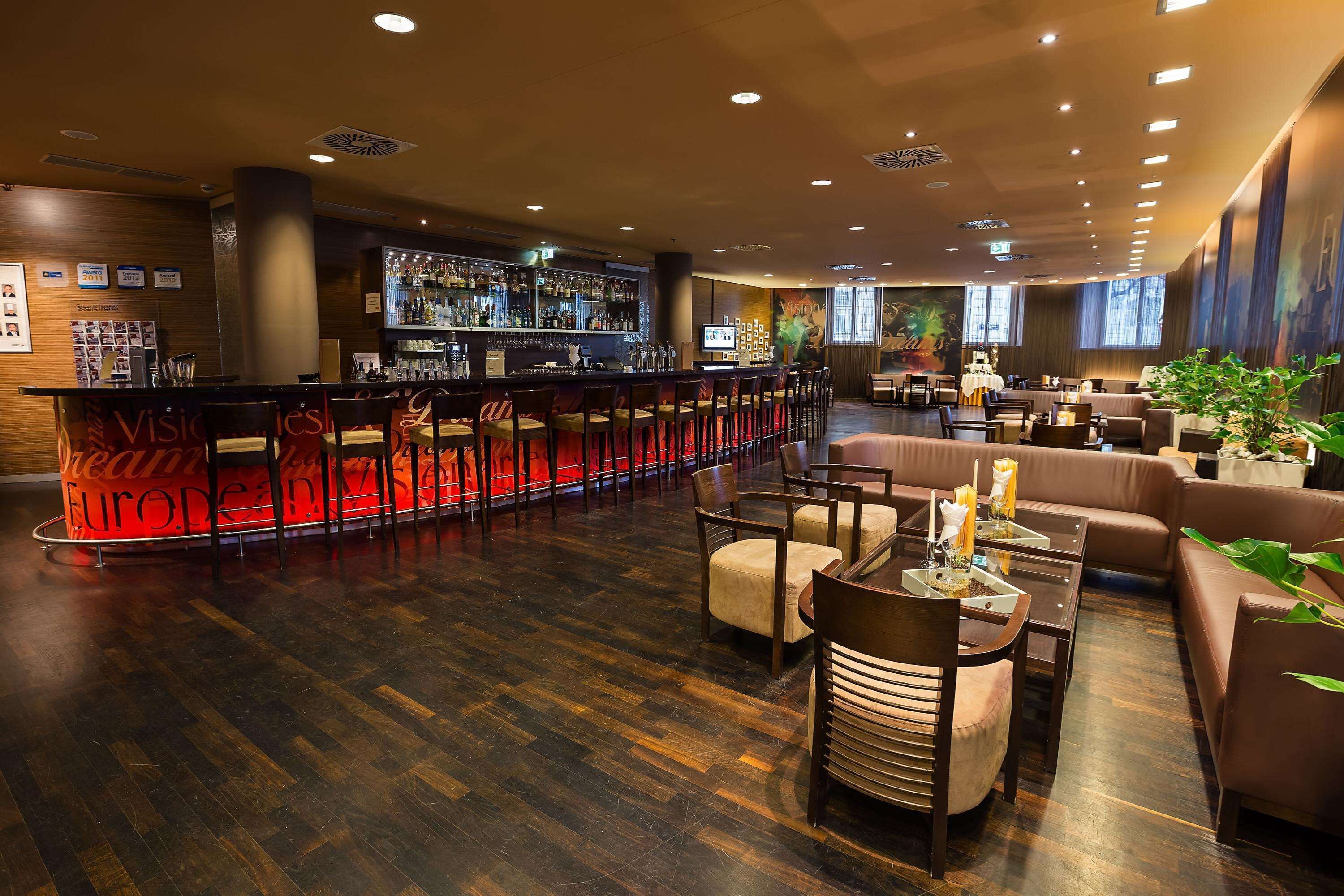 A bar area with a long counter, multiple bar stools, and a seating area with couches and tables.