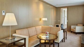 Quarto de hotel moderno com sofá de couro bege, mesa de centro de vidro, abajur e mesa lateral.