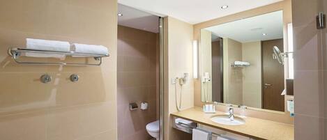 Un baño moderno con cabina de ducha de vidrio, inodoro, lavamanos con espejo y toallero.