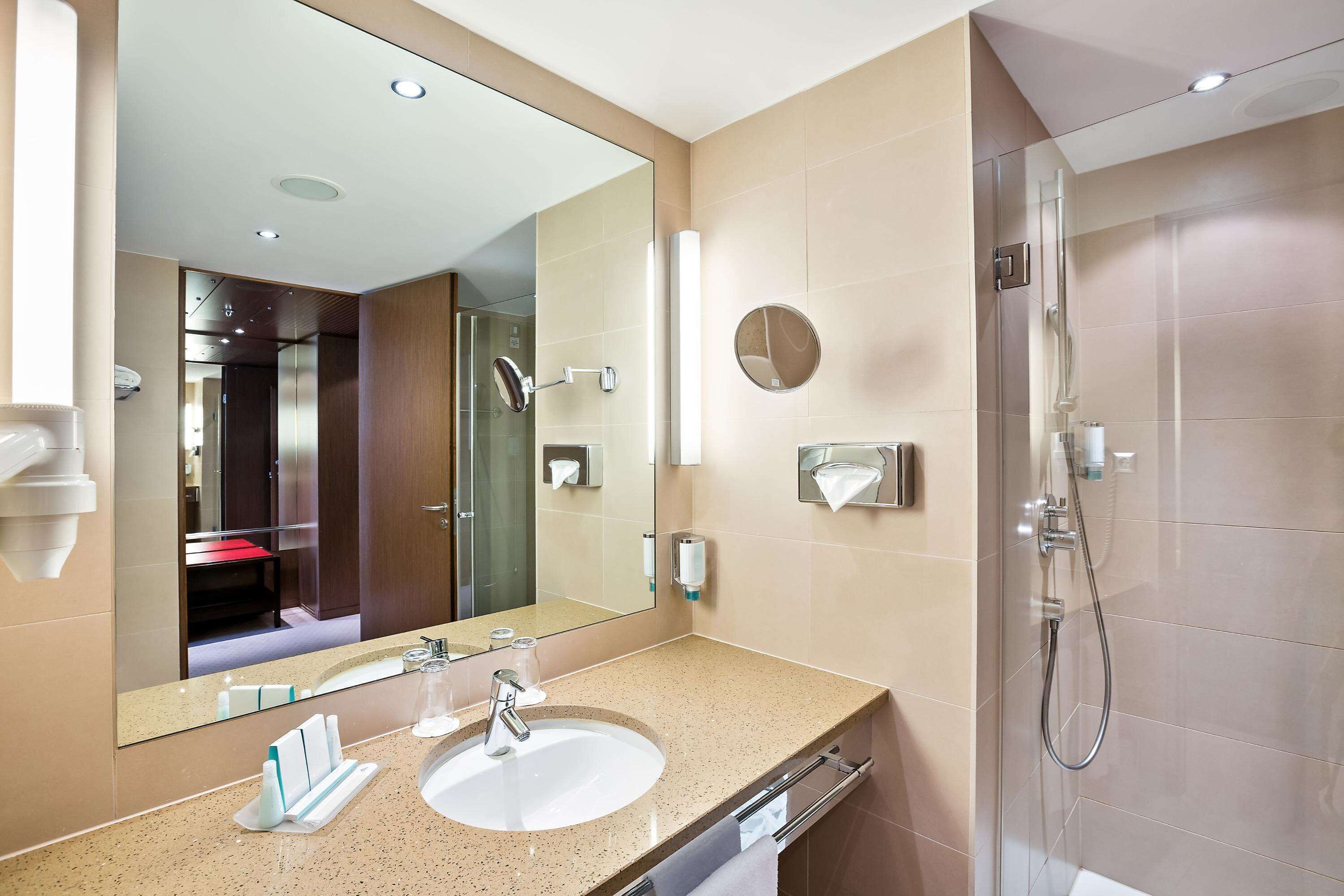 A modern bathroom with a large mirror, a sink, and a shower.