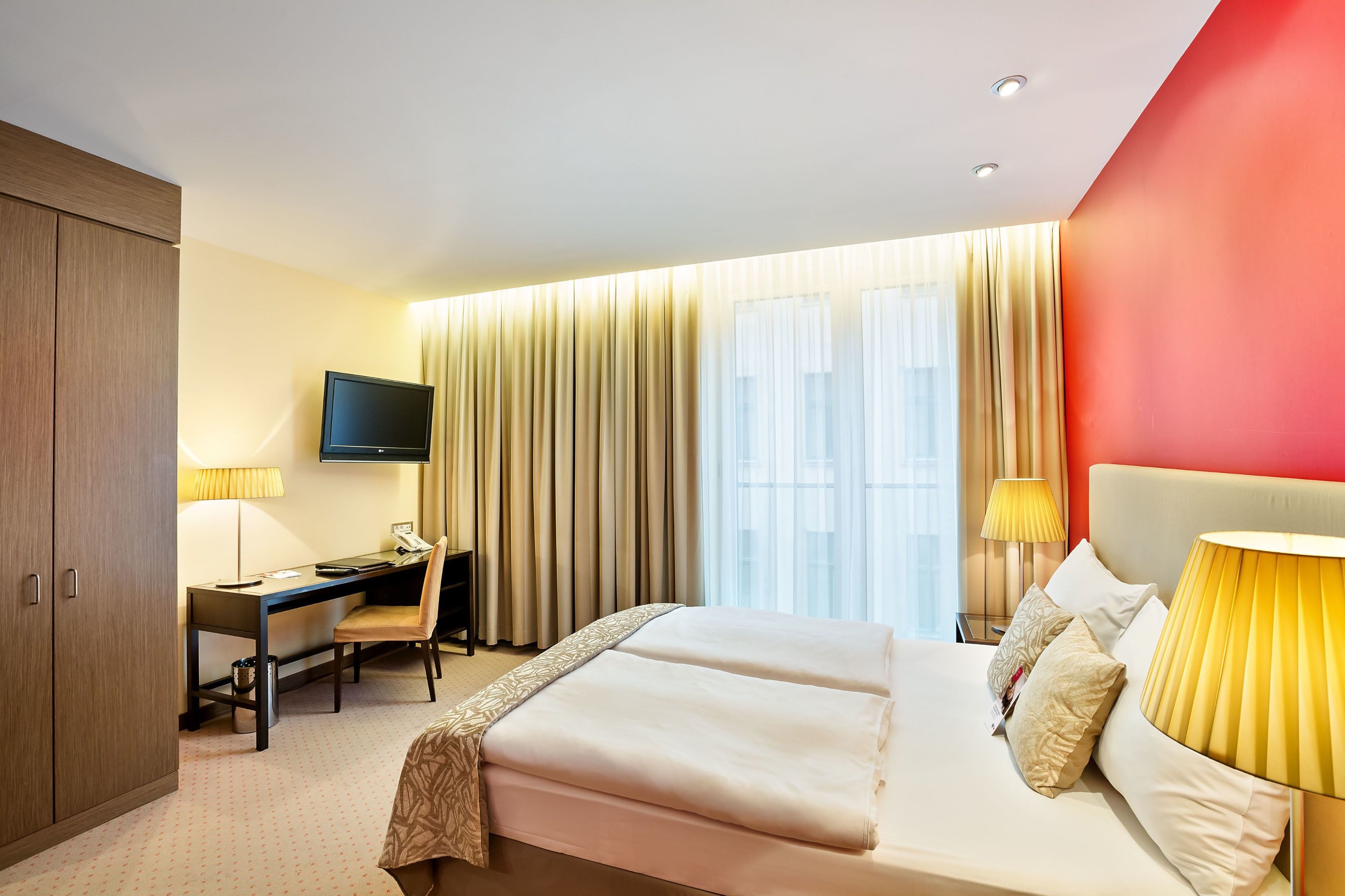 A hotel room with a bed, desk, chair, TV, and curtains.
