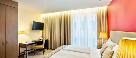 A hotel room with a bed, desk, chair, TV, and curtains.