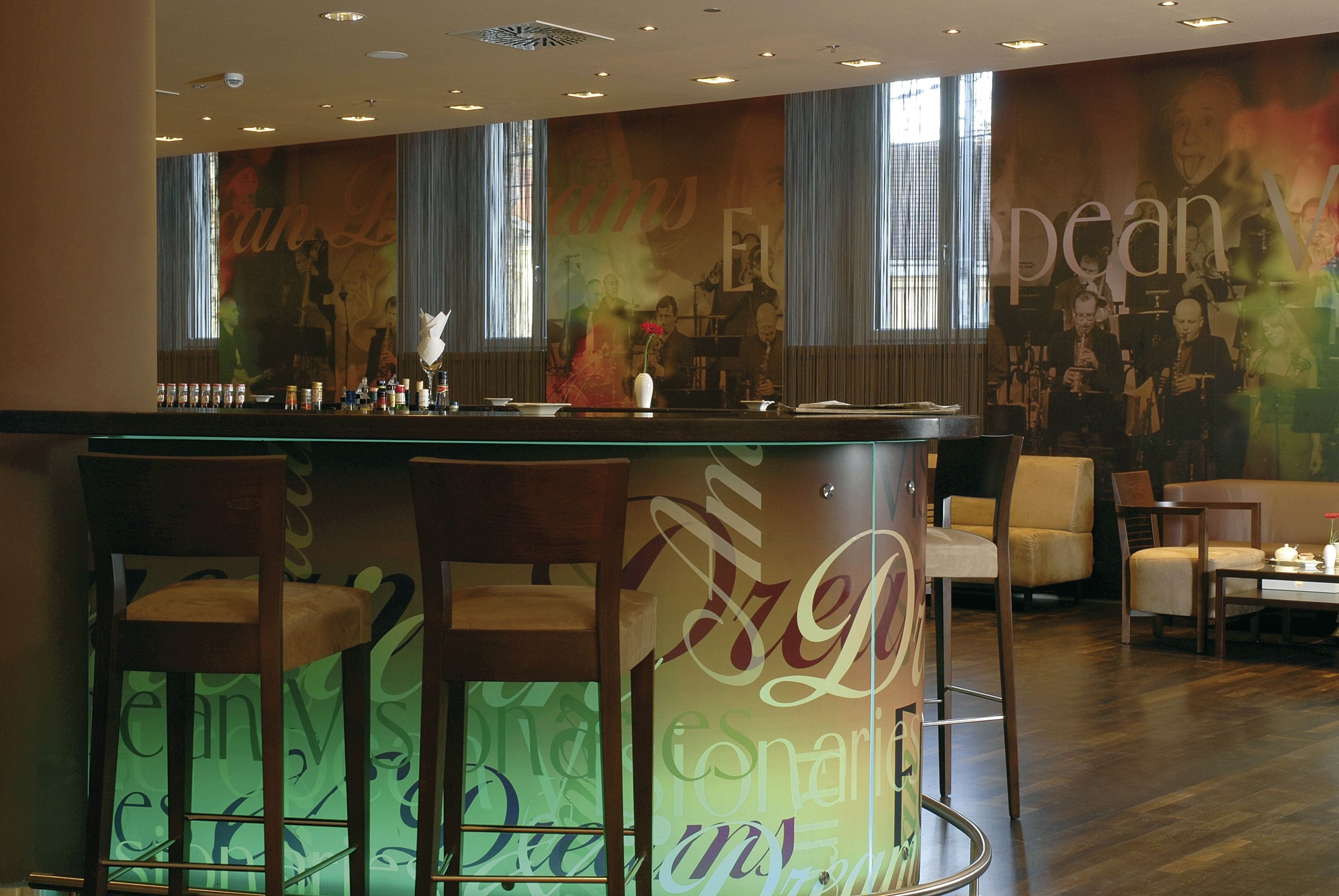 Uma área de bar com balcão, banquetas e um mural com texto e imagens.