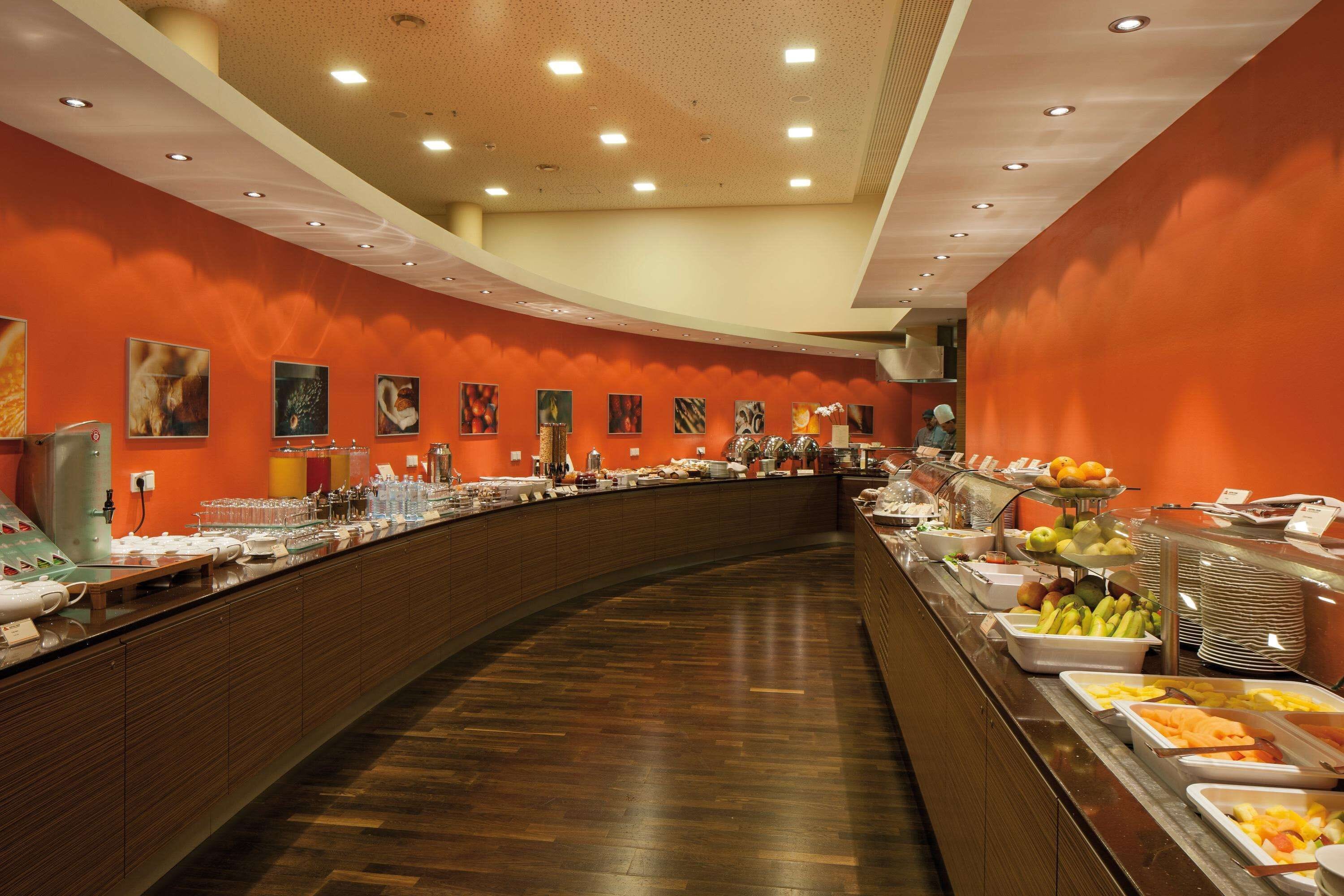 Uma área de buffet com balcão curvo, diversos alimentos e obras de arte nas paredes.