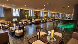 A spacious hotel lobby with multiple seating areas, a bar, and a large mural on the wall.