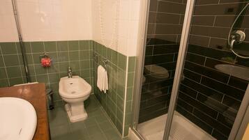 A bathroom with a shower, toilet, bidet, and sink.