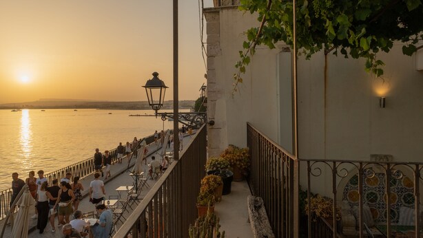 A riverside walkway with people walking and sitting, overlooking a body of water. - Charme Hotel Henry's House (Syracuse)