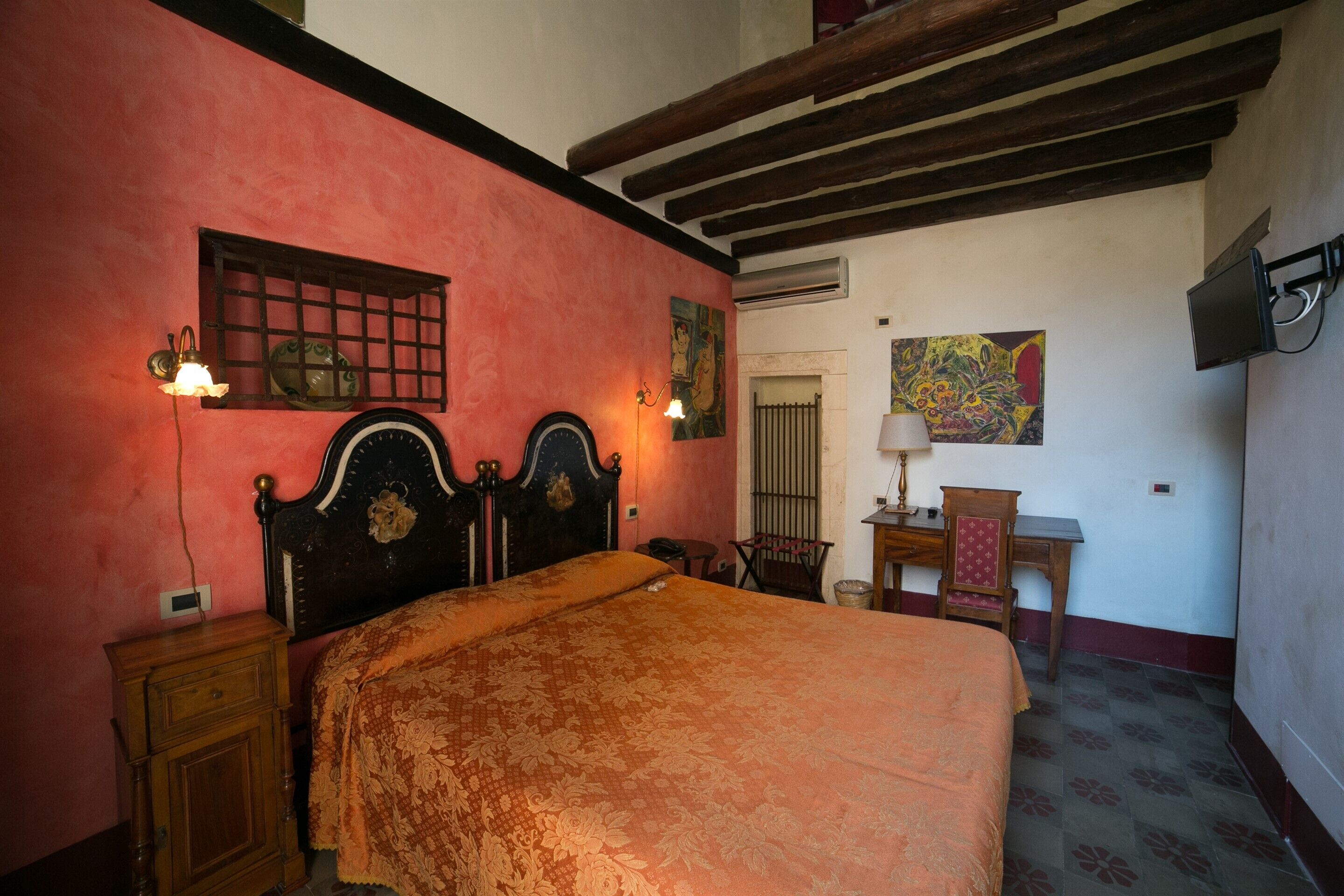A bedroom with a large bed, wooden headboard, a nightstand, a desk, a chair, and a painting on the wall.