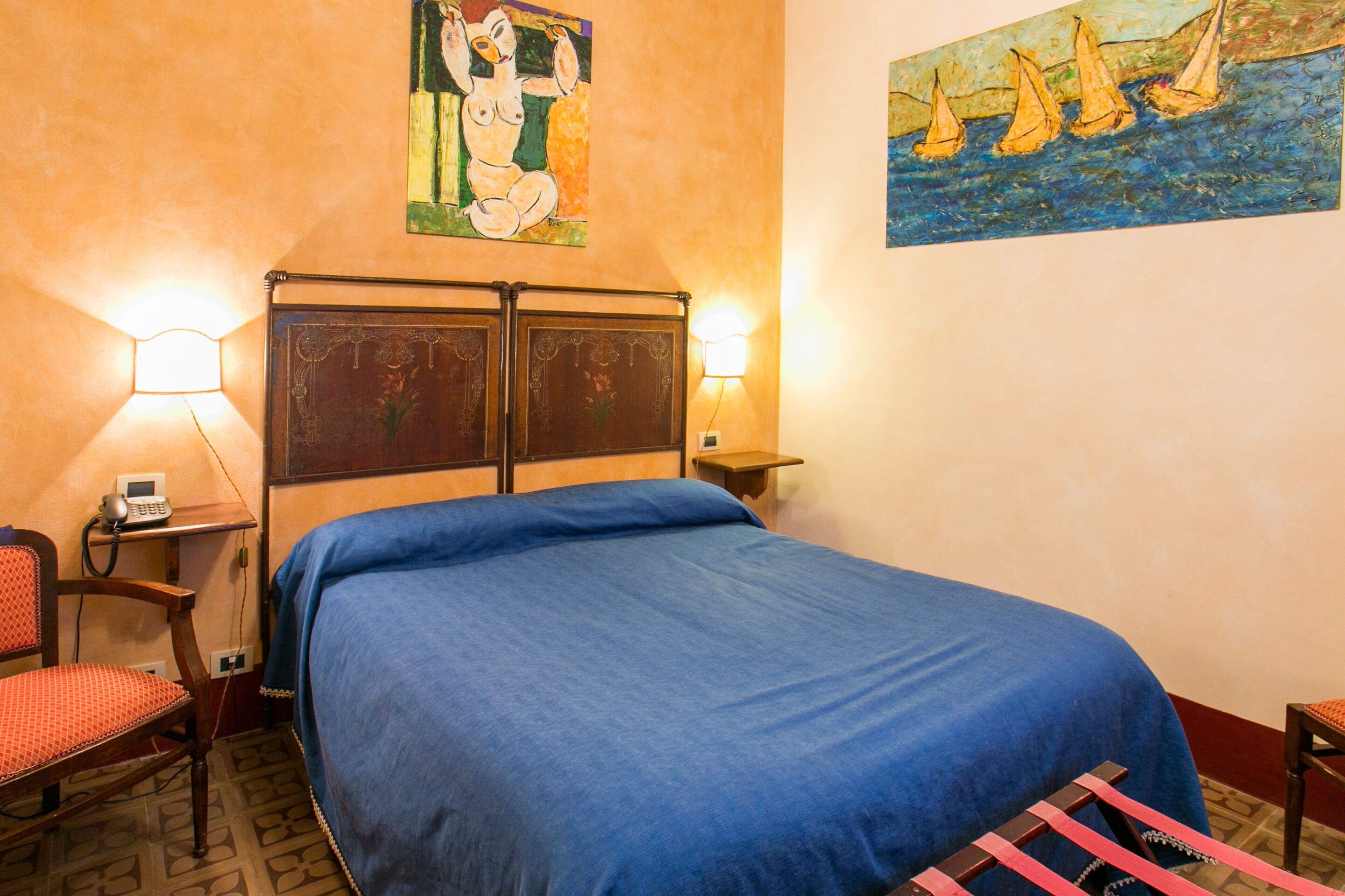 Una habitación de hotel con una cama grande, dos lámparas de noche, una silla y obras de arte en las paredes.