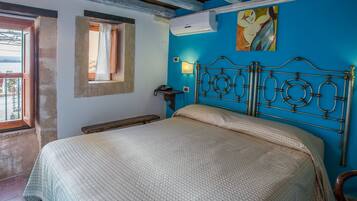 Un dormitorio con cama, mesita de noche, aire acondicionado instalado en la pared, un cuadro y ventana con cortina.