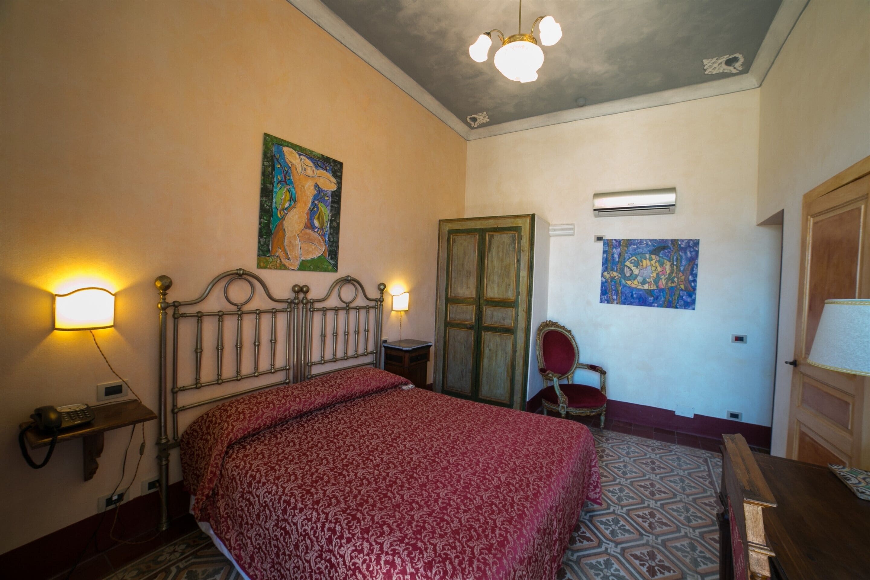 A bedroom with a bed, a wooden wardrobe, a chair, and a painting on the wall.