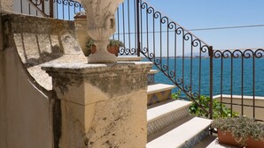 A stone staircase with a large urn on the landing, leading to a balcony with a metal railing overlooking the sea. - Charme Hotel Henry's House (Syracuse)