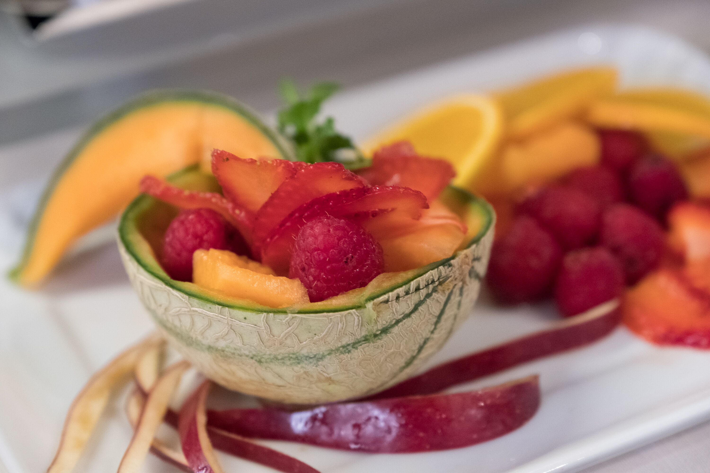 A bowl of fruit including melon, strawberries, and raspberries.