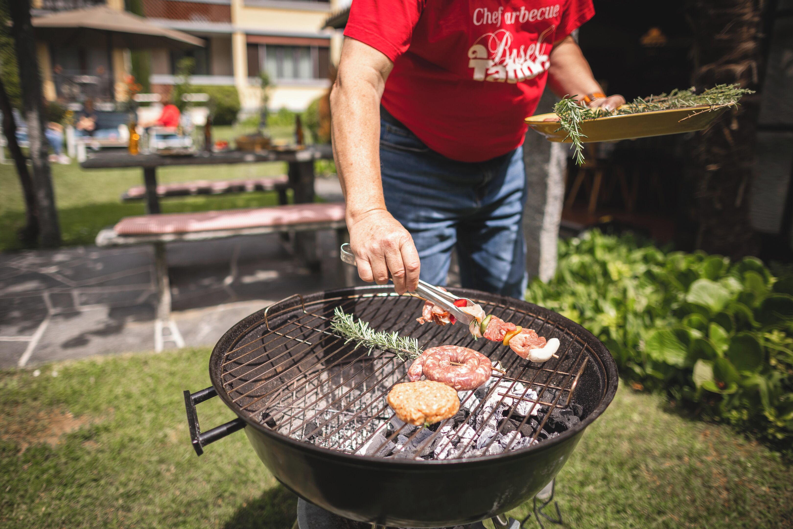 Une personne qui fait griller des saucisses et un hamburger sur un barbecue extérieur.