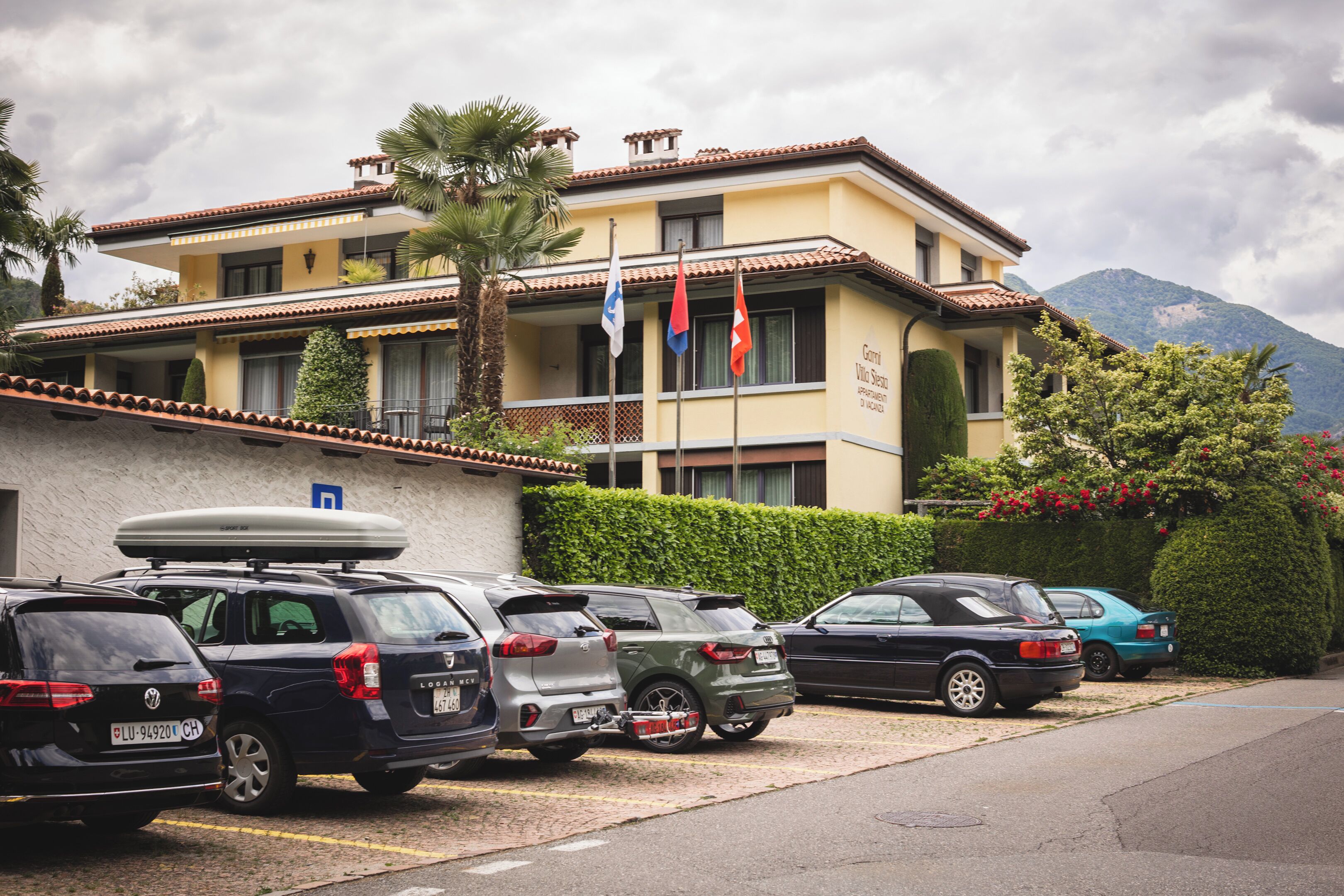A hotel with a parking lot, multiple cars, and flags.