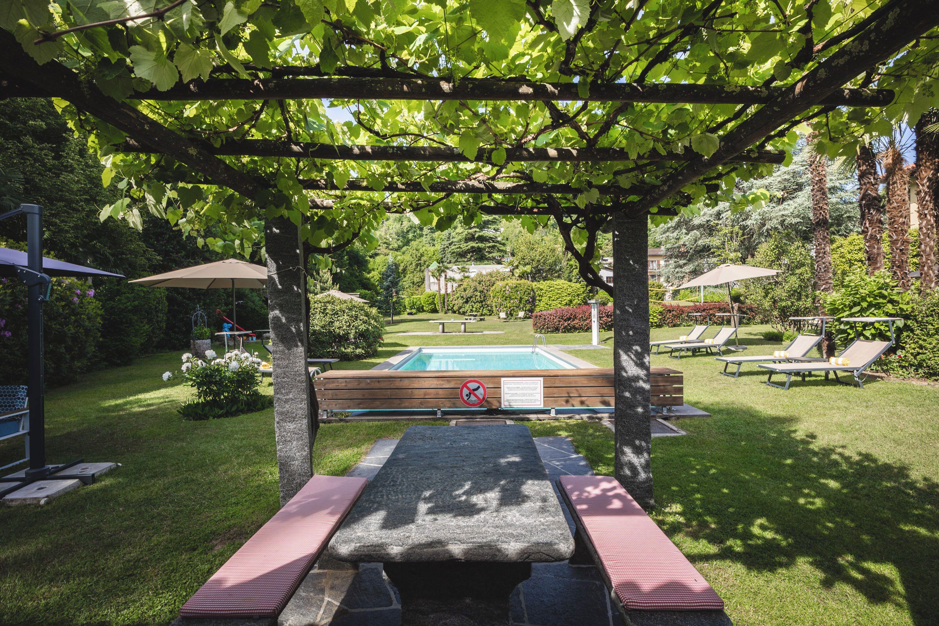 A pool area with lounge chairs and a table under a pergola.