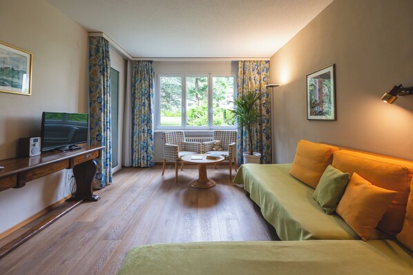 Una habitación con cama, escritorio con computadora, silla, mesa y ventana con cortinas.