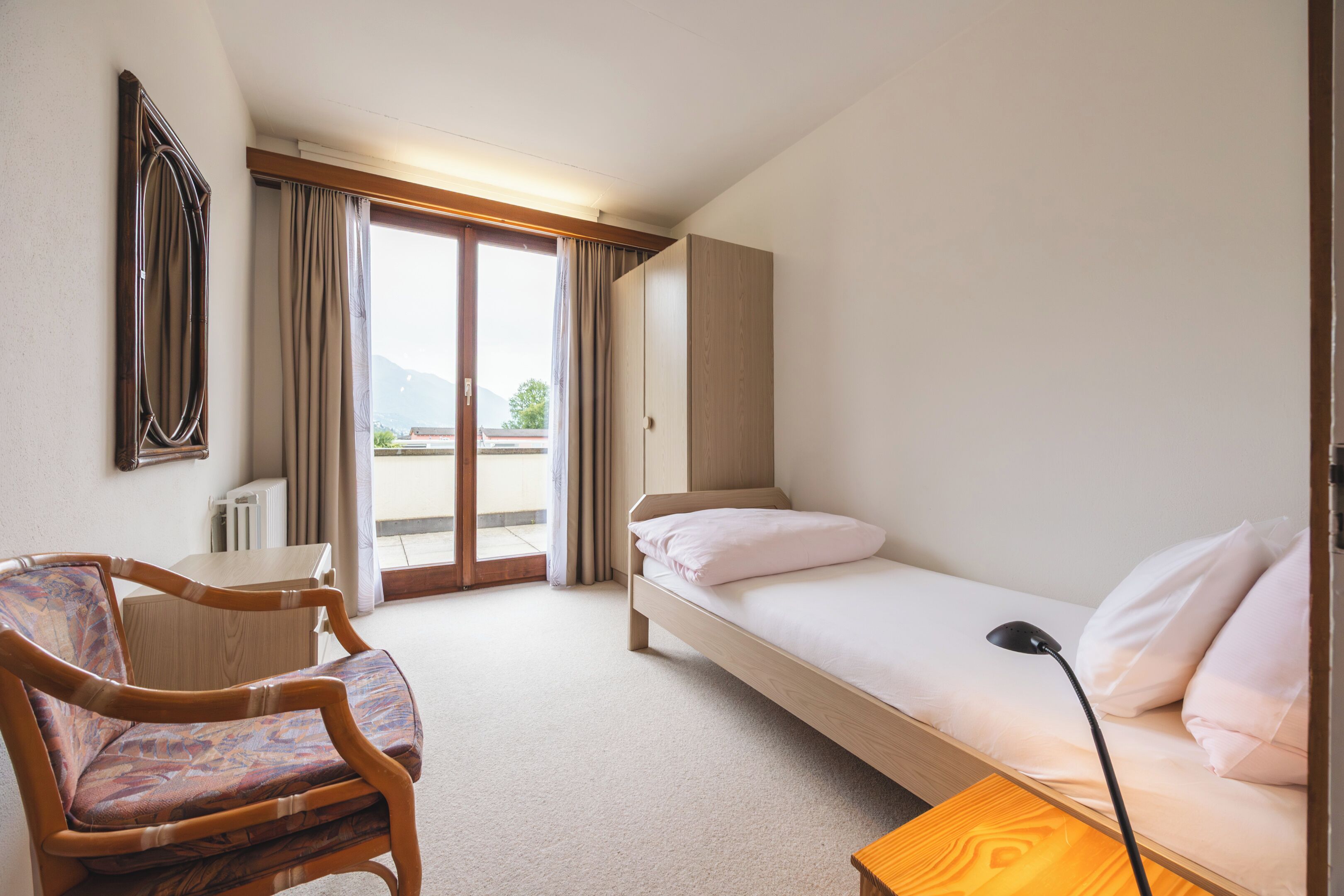 Ein Hotelzimmer mit Bett, Sessel, Schreibtisch und Blick ins Freie.