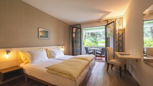 A hotel room with a bed, bedside tables, a desk, and a chair. - Villa Siesta, Park & Pool Living (Losone)