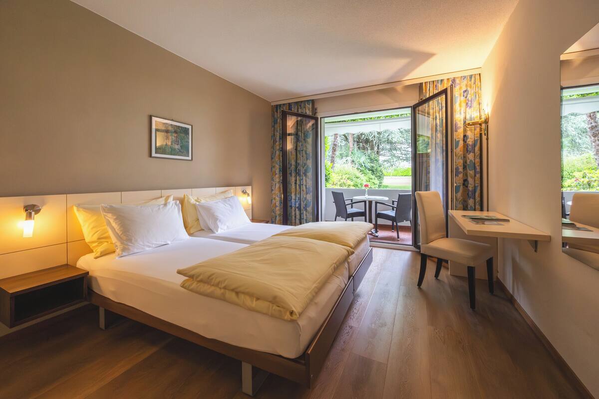 Quarto de hotel com cama, mesas de cabeceira, escrivaninha e uma cadeira.