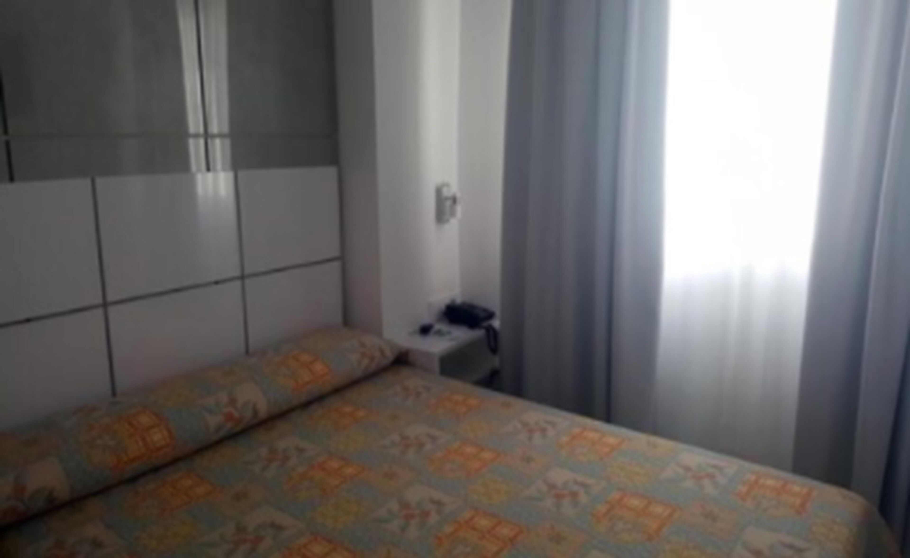 Ein Hotelzimmer mit einem Bett, einem kleinen Nachttisch und einem Fenster mit Vorhängen.