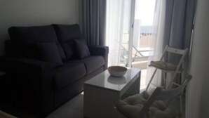 A living room with a dark-colored sofa, a white coffee table, and a white chair. - Hotel Sol Playa (Valencia)