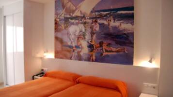 Camera d'albergo con un grande quadro raffigurante una spiaggia, un letto con copriletto arancione e lampade da comodino.