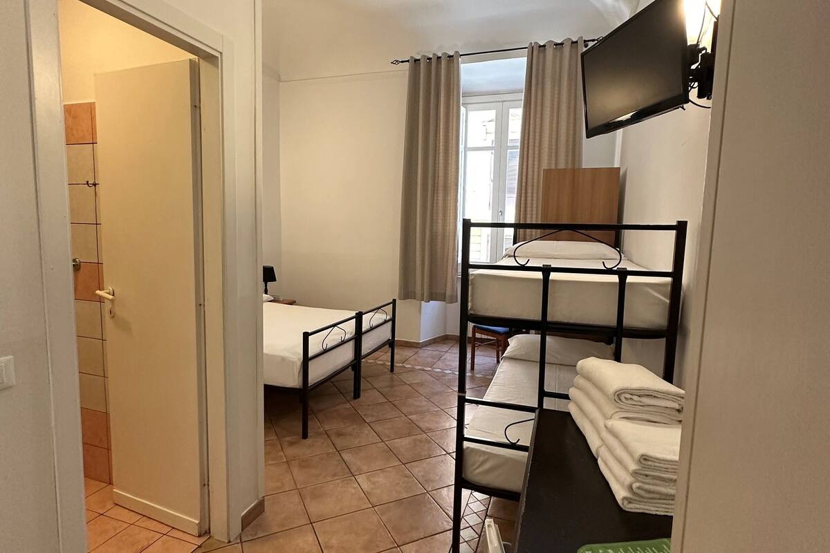 A hotel room with a bunk bed, a desk with a chair, a flat-screen TV, and a bathroom with a shower and toilet.