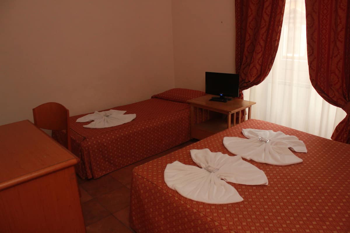 A hotel room with two single beds, a desk with a computer, a chair, and a TV.