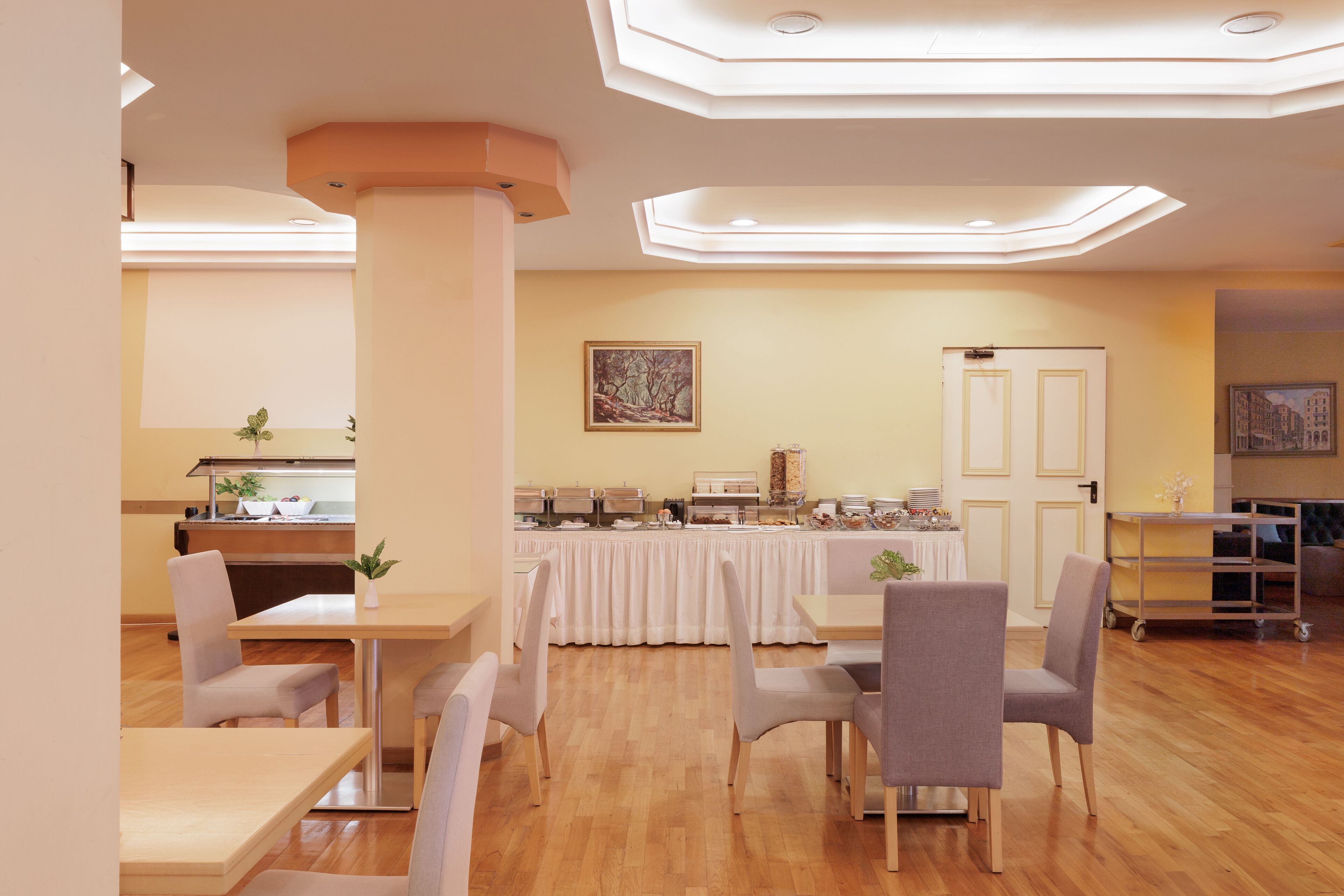 Ein Essbereich mit Tischen und Stühlen, ein Buffet mit Speisen sowie eine Tür im Hintergrund.
